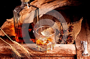 Glass of whiskey with ice decanter on wooden table