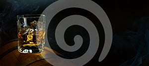 Glass of whiskey with ice on an oak barrel and the smoke of a Cuban cigar on a dark background. Men`s club banner idea. Copy