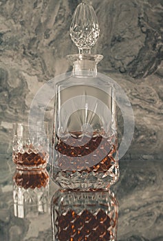 Glass of whiskey with ice and a square decanter isolated on a dark background