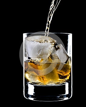Glass of whiskey and ice under the pouring whiskey