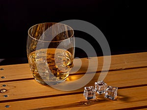Glass of whiskey with ice on a wooden table.