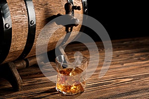 Glass of whiskey near barrel on wooden table