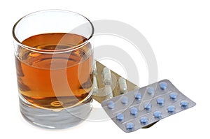 Glass of whiskey next to blister packs of drugs on white background