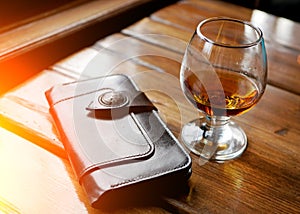 Glass of whiskey or other strong amber alcoholic beverage and leather brown purse on black reflecting table top studio background
