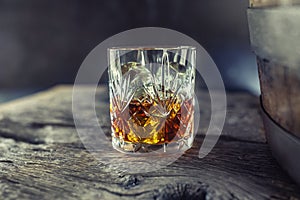 Glass with whiskey rum brandy or bourbon on an old table near a wooden barrel