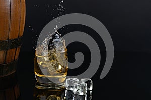 Glass of whiskey with splash, on a black background. old barrel. ice