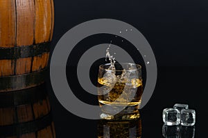 Glass of whiskey with splash, on a black background. old barrel. ice