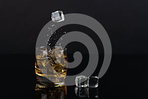 Glass of whiskey with splash, on a black background. old barrel. ice