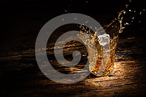 A glass of whiskey with splashes from the ice cube. glass with a splash of whisky on wooden background