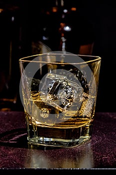 Glass of whiskey on wood table with bottles in background, warm atmosphere photo