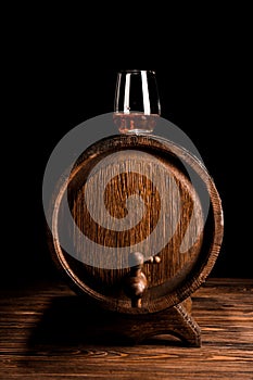 Glass of whiskey on wooden barrel against black background