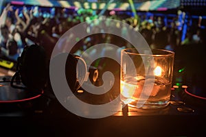 Glass with whisky with ice cube inside on dj controller at nightclub. Dj Console with club drink at music party in nightclub with