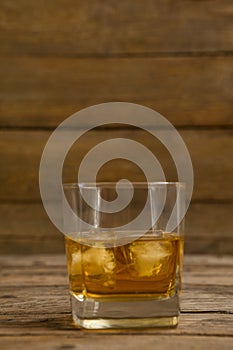 Glass of whisky with ice cube on wooden table