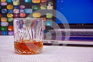 A GLASS OF WHISKEY AND LAPTOP SHOT ON A COLORFUL BACKGROUND