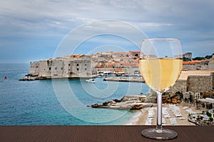 Glass of white wine against Dubrovnik background. Vacation concept. Beach and city wall in historic center of Dubrovnik, Croatia