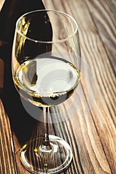 Glass of white wine and bottle on wooden background, selective focus