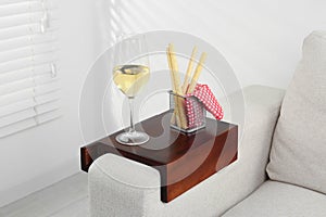 Glass of white wine and breadsticks on sofa with wooden armrest table in room. Interior element
