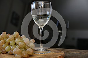 Glass of white wine and bunch of grapes on a wooden table. With copy space for text.