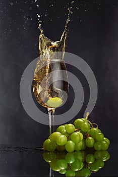 A glass of white wine on a dark background. Splash white wine. Grape bunch