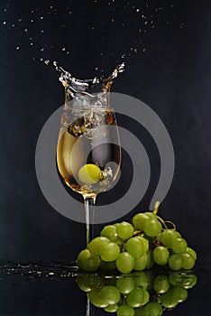 A glass of white wine on a dark background. Splash white wine. Grape bunch