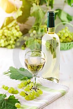 A glass of white wine, fresh grapes and a bottle of white wine on a wooden table.