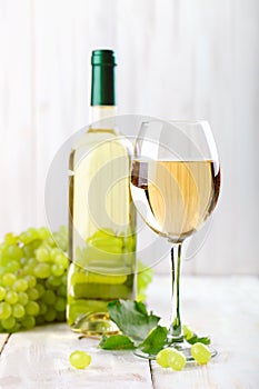 A glass of white wine, fresh grapes and a bottle of white wine on a wooden table.