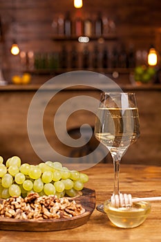 Glass of white wine with fresh grapes and wolnuts on a wooden plate in a vintage restaurant