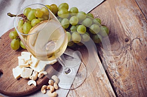 Glass of white wine, grapes, cashew nuts and soft cheese