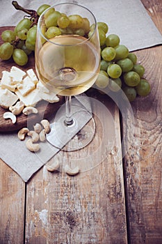 Glass of white wine, grapes, cashew nuts and soft cheese