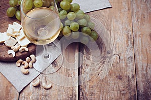 Glass of white wine, grapes, cashew nuts and soft cheese