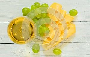 Glass of white wine, grapes and cheese on a plate on a white wooden background. Top view.