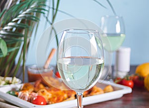 Glass of white wine and homemade food chicken tabaka with vegetables on the baking sheet on the background. Dinner concept