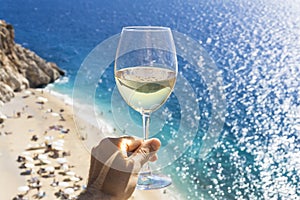 A glass of white wine in a man`s hand. Wine against the backdrop of the sea coast and a sunny summer beach. Wine tasting and