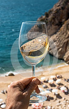 A glass of white wine in a man`s hand. Wine against the backdrop of the sea coast and a sunny summer beach. Wine tasting and
