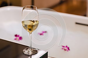 A glass of white wine puts on table beside bathtub