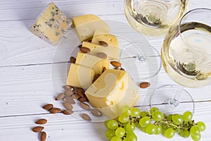 Glass of white wine with snacks - various types of cheese, figs, nuts, honey, grapes on a wooden boards background