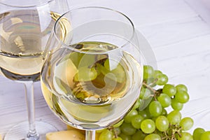 Glass of white wine with snacks - various types of cheese, figs, nuts, honey, grapes on a wooden boards background