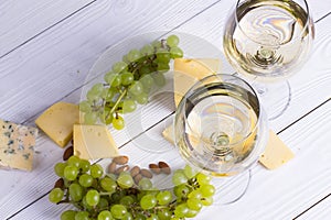 Glass of white wine with snacks - various types of cheese, figs, nuts, honey, grapes on a wooden boards background