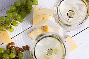 Glass of white wine with snacks - various types of cheese, figs, nuts, honey, grapes on a wooden boards background