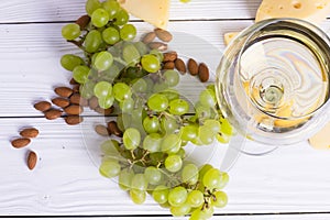 Glass of white wine with snacks - various types of cheese, figs, nuts, honey, grapes on a wooden boards background