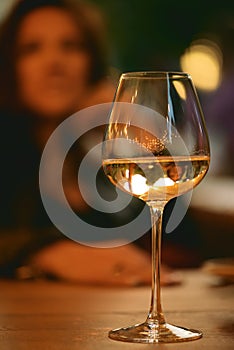 Glass of white wine on table on background of unrecognizable woman sitting in cafe or restaurant. Focus on wine glass