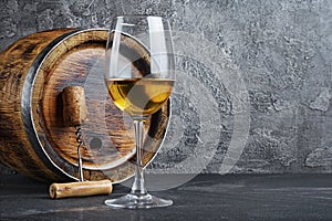 Glass with white wine for tasting and wooden barrel with corkscrew in dark cellar