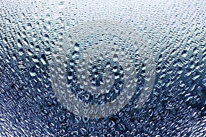 Glass window in raindrops, beautiful blue gradient color with water drops, misted mirror surface texture background close up