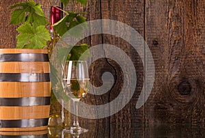 Glass of wine with barrel white bottle behind grapeleaves