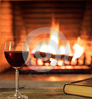 Glass of wine and a book, logs burning in a fireplace