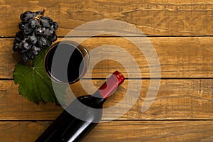 Glass with wine bottle grapes and vine leaf on wooden background. Top view with copy space