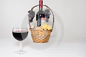 A glass of wine. A bottle of red wine, grapes and picnic basket with cheese slices on white background.