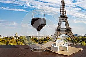 Glass of wine with brie cheese on Eiffel tower and Paris skyline background. Sunny view of glass of red wine overlooking the