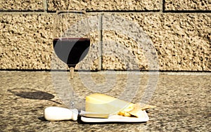 Glass of wine with cheddar cheese, small knife, and crackers on an outdoor table