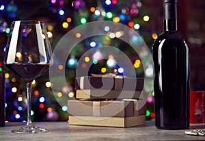 Glass of wine and gift boxes on table, blurred christmas lights in the background